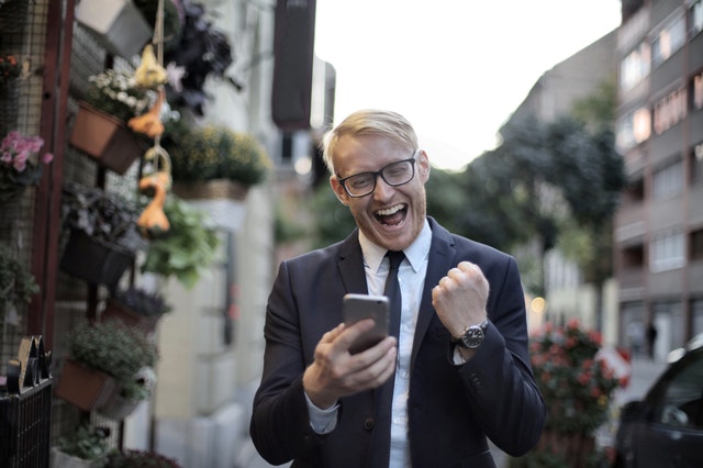 man in a suit with a big smile while holding phone and clenching fist